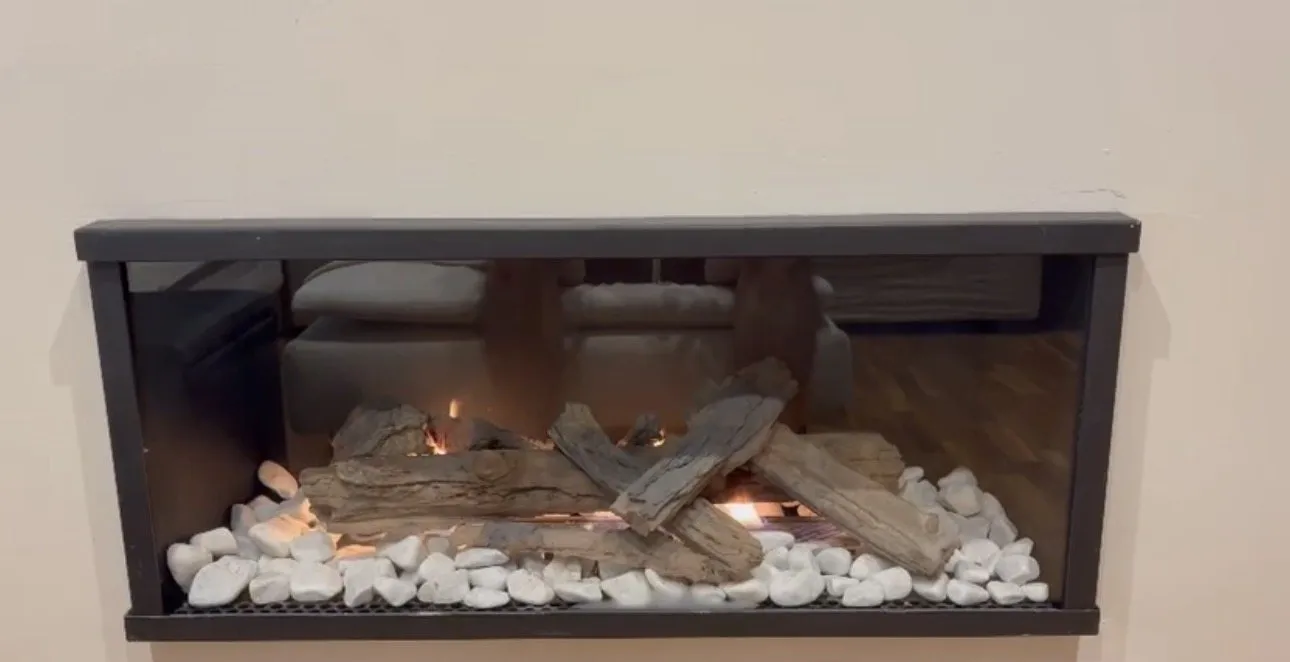 Chimenea de gas Lisboa a 1 cara con troncos y piedras blancas, en casa de un cliente