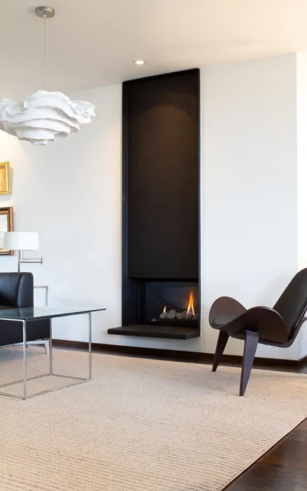Chimenea de gas Berlín empotrada en un muro alto negro de un salón blanco